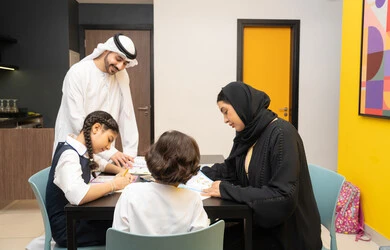 الاهتمام بتعليم بالأبناء ودعمهم، الانشطة التعليمية وتنمية القدرات، زوجان عربيان خليجيان اماراتيان يرتديان الزي التقليدي يجلسان على الطاولة يقومان بتعليم ابنائهم، استغلال أوقات الفراغ بالأنشطة الترفيهية الممتعة