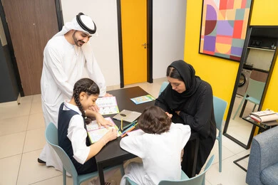 الانشطة التعليمية وتنمية القدرات، مساعدة الابناء في تأدية الواجبات المدرسية، زوجان عربيان خليجيان اماراتيان يرتديان الزي التقليدي يجلسان على الطاولة يقومان بتعليم ابنائهم، استغلال أوقات الفراغ بالأنشطة الترفيهية الممتعة