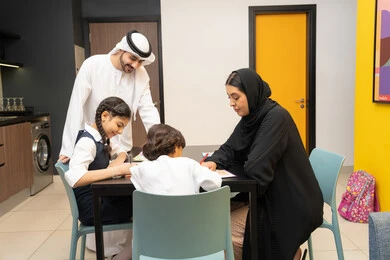 Utilizing free time with fun recreational activities, developing children's abilities, an Emirati Gulf Arab couple wearing traditional dress sitting at a table teaching their children, educational activities, teaching, developing and caring for children