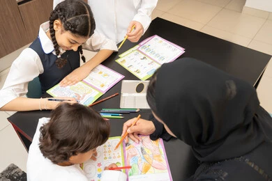 تنمية قدرات الطفل، صورة مقربة لام عربية خليجية اماراتية ترتدي العباءه السوداء تجلس على الطاولة تقوم بتعليم ابنائها، الانشطة التعليمية، تعليم وتطوير والاهتمام بالابناء، استغلال أوقات الفراغ بالأنشطة الترفيهية الممتعة