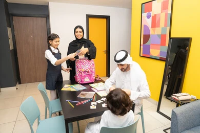 البهجة بالعودة إلى المدرسة, عائله عربيه خليجيه اماراتية تقوم بالاستعداد و التحضير لبداية عام دراسي جديد، ام خليجيه ترتدي العباءه السوداء تقوم بوضع الكتب و الدفاتر داخل الحقيبة المدرسية برفقه ابنتها, اب عربي خليجي يرتدي الكندورة و الغتره يجلس مع ابنه على الطاوله