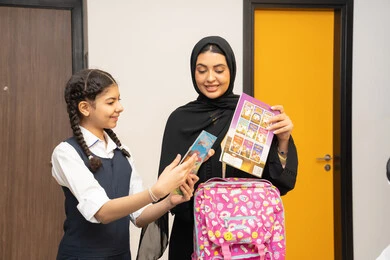 تعلم وتطوير الابناء، الاستعداد لبدء عام دراسي جديد، الاهتمام بتعليم بالأبناء ودعمهم ، مفهوم التعلم في المدارس المتطورة في الامارات العربية، أم عربية خليجية اماراتية محجبة ترتدي عباءة سوداء تقوم بمساعدة ابنتها بتحضير الحقيبة المدرسية