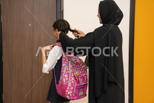 العاطفة عند الأمهات، الاستعداد لبدء عام دراسي جديد، المثابرة والاجتهاد للوصول الى المراتب العليا، مفهوم التعلم في المدارس المتطورة في الامارات العربية،صورة من الخلف لأم عربية خليجية اماراتية محجبة ترتدي عباءة سوداء تقوم بتوضيب شعر ابنتها