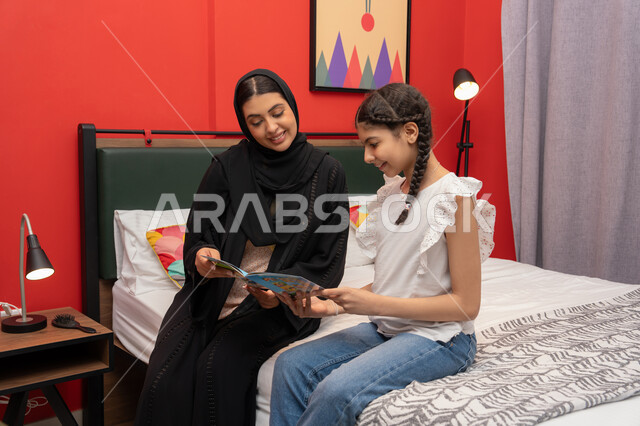 الإستمتاع بالأنشطه الترفيهية وقضاء الوقت مع الاولاد، تعزيز الروابط العائلية، ام سعودية تقوم بقضاء وقت ممتع مع الابنه، المشاركه بقراءه القصص المفيده مع الأبناء قبل النوم، بامراة عربيه خليجيه اماراتية ترتدي العباءه السوداء تجلس على السرير برفقه ابنتها تقرأ الروايات المسليه