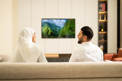 The discussion about the presented topic, watching television and enjoying spending time with family, the concept of bonding and family understanding, a Saudi Arabian couple sitting on a comfortable sofa watching TV channels and programs, sitting in the living room, enjoying leisure time with the wife.