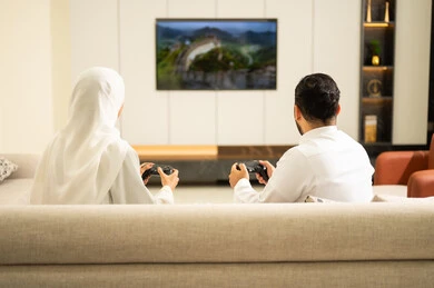 مفهوم الأسرة السعيدة, لعب العاب الفيديو الترفيهية ، قضاء أوقات الفراغ مع العائلة ، استخدام التكنولوجيا الحديثة، صورة من الخلف لزوجان عربيان خليجيان سعوديان يمسكان عصا التحكم، إيماءات الفوز والخسارة فى اللعبة، التفاعل والاندماج مع الالعاب الالكترونية .