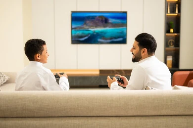 مفهوم الأسرة السعيدة، قضاء أوقات الفراغ مع العائلة، أب وإبن سعودي خليجي عربي بزي التقلدي يمسكان عصا التحكم و يلعبان بألعاب الفيديو، إيماءات تدل على الإندماج والتفاعل مع اللعبه، المتعة و التسلية بألعاب الفيديو، ألعاب البلايستيشن الترفيهية، اللعب مع الأطفال