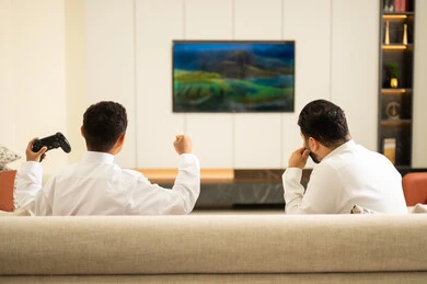 قبضة يد تدل على الفوز، قضاء أوقات الفراغ مع العائلة، أب وإبن سعودي خليجي عربي بزي التقلدي يمسكان عصا التحكم و يلعبان بألعاب الفيديو، إيماءات تدل على الإندماج والتفاعل مع اللعبه، المتعة و التسلية بألعاب الفيديو، ألعاب البلايستيشن الترفيهية، اللعب مع الأطفال