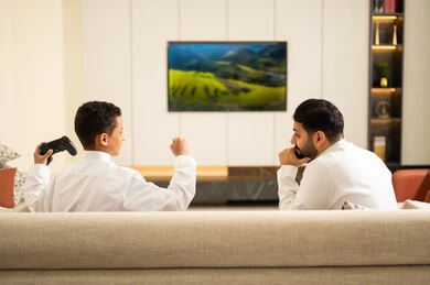 اللعب مع الأطفال، قبضة يد تدل على الفوز، قضاء أوقات الفراغ مع العائلة، أب وإبن سعودي خليجي عربي بزي التقلدي يمسكان عصا التحكم و يلعبان بألعاب الفيديو، إيماءات تدل على الإندماج والتفاعل مع اللعبه، المتعة و التسلية بألعاب الفيديو، ألعاب البلايستيشن الترفيهية