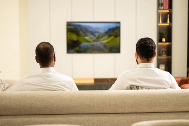 الجلوس في غرفة المعيشة على آريكة مريحة، الشغف بمتابعة المباريات، ايماءات الحماس بالفوز وتسجيل الأهداف، قضاء وقت ممتع مع الأصدقاء في المنزل، صورة من الخلف لصديقان عربيان خليجيان سعوديان يشاهدان مباراة كرة القدم في غرفة المعيشة