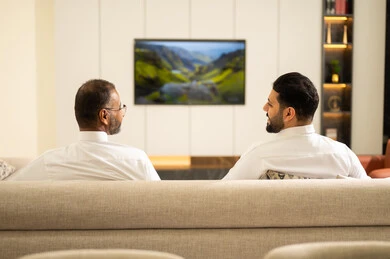 The passion for following the matches, gestures of excitement for winning and scoring goals, spending enjoyable time with friends at home, two Arab Gulf friends from Saudi Arabia watching a football match in the living room, sitting in the living room on a comfortable sofa, excitement and interaction with the national team.
