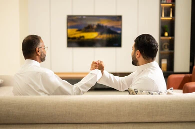 الحماس والتفاعل مع المنتخب، الشغف بمتابعة المباريات، ايماءات الحماس بالفوز وتسجيل الأهداف، قضاء وقت ممتع مع الأصدقاء في المنزل، صديقان عربيان خليجيان سعوديان يشاهدان مباراة كرة القدم في غرفة المعيشة، الجلوس في غرفة المعيشة على آريكة مريحة