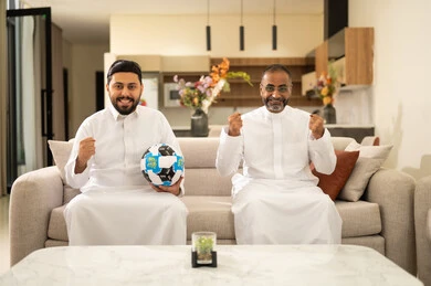الحماس والتفاعل مع المنتخب، الشغف بمتابعة المباريات، ايماءات الحماس بالفوز وتسجيل الأهداف، قضاء وقت ممتع مع الأصدقاء في المنزل، صديقان عربيان خليجيان سعوديان يشاهدان مباراة كرة القدم في غرفة المعيشة، الجلوس في غرفة المعيشة على آريكة مريحة