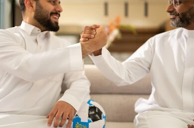 أيدي مشجعين في لحظة فوز، أنديه رياضية مختلفة، ايماءات الحماس بالفوز وتسجيل الأهداف، قضاء وقت ممتع مع الأصدقاء في المنزل، صورة مقربة من الخلف لصديقان عربيان خليجيان سعوديان يشاهدان مباراة كرة القدم في غرفة المعيشة، الجلوس في غرفة المعيشة على آريكة مريحة