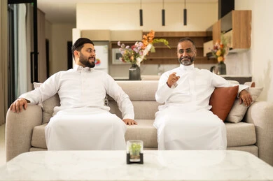 المناقشة والحوار بين الأصدقاء، التسليه والترفيه الشبابي, قضاء وقت ممتع مع الأصحاب، صديقان عربيان خليجيان سعوديان يرتديان الثوب التقليدي يجلسان على آريكه مريحة باللون الابيض، الاستمتاع بالأنشطة الترفيهيه في عطلة نهاية الاسبوع