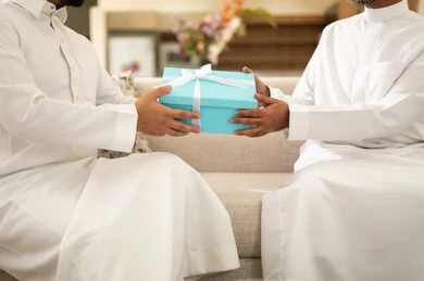 رجل يقدم هدية لصديقه بمناسبة خاصة، قضاء وقت ممتع مع الأصحاب، المناقشة والحوار بين الأصدقاء، التسليه والترفيه الشبابي,  صورة مقربة لأيدي صديقان عربيان خليجيان سعوديان يرتديان الثوب التقليدي يجلسان على آريكه مريحة ، قضاء وقت ممتع في المنزل مع الأصدقاء
