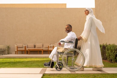 التنزه في الهواء الطلق،جودة حياة ذوي الهمم في السعودية ، الاخلاص والعطف بين الزوجين، تأمين أدوات ومعدات لمساعدة المرضي ، رجل مقعد يجلس على كرسي متحرك، امرأة عربية خليجية سعودية ترتدي العباءة والحجاب تساعد زوجها على التنقل والحركة.