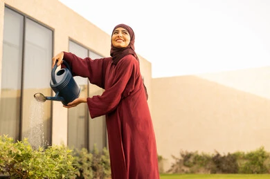 المتعة و التسليه ،النظر الى الأعلى بايماءات السعادة، مفهوم النظافة والاهتمام بحديقة المنزل، امرأة عربية خليجية سعودية تقوم باستخدام وعاء السقي، امرأة عربية خليجية عمانية تقوم بري النباتات بالرش  ،أجواء الطبيعة الخلابة ، قضاء الوقت الممتع في إحدى الشاليهات .