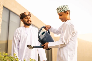 ايماءات السعادة على وجوههم، المشاركة مع الاولاد في المهم اليومية، قضاء الوقت الممتع في إحدى الشاليهات ، مفهوم النظافة والاهتمام بحديقة المنزل ، رجل عربي خليجي عماني يقضي وقت ممتع مع إبنه في ري النباتات بإستخدام وعاء السقي ، فعاليات وأجواء ترفيهية .