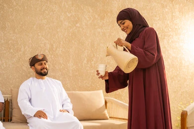 الاستمتاع وشرب القهوة العربية، اجواء مليئة بالمحبة والود، التنزه في الهواء الطلق، مفهوم العلاقات الزوجية الناجحة السعيده، قضاء عطلة نهاية الاسبوع في أحد الشاليهات السياحية ،زوجان عربيان خليجيان عمانيان يرتديان الزي التقليدي يقومان بتبادل الأحاديث والدردشات