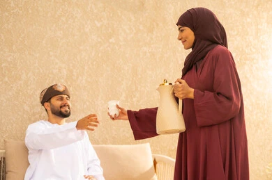 اجواء مليئة بالمحبة والود، الاستمتاع وشرب القهوة العربية، التنزه في الهواء الطلق، مفهوم العلاقات الزوجية الناجحة السعيده، قضاء عطلة نهاية الاسبوع في أحد الشاليهات السياحية ،زوجان عربيان خليجيان عمانيان يرتديان الزي التقليدي يقومان بتبادل الأحاديث والدردشات