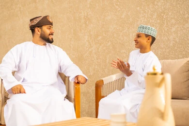 عطلة صيفية وأجواء عائلية سعيدة ، اللعب و التسلية مع الابناء, التنزه في الهواء الطلق، عائلة عربية خليجية عمانية تقضي أوقات ممتعة في إحدى الشاليهات السياحية بالسلطنة, رجل عربي خليجي عماني يرتدي الدشداشة والعمامة يقوم بمحادثة ابنه