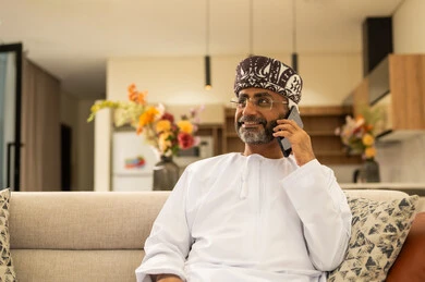 Making a phone call, using a modern and advanced technical device, browsing social media sites on the internet, communicating and chatting with friends and relatives via mobile, an Arab Gulf Omani man wearing a dishdasha and turban sitting in the living room holding a mobile phone in his hand. Making a phone call, using a modern and advanced technical device, browsing social media sites on the internet, communicating and chatting with friends and relatives via mobile, an Arab Gulf Omani man wearing a dishdasha and turban sitting in the living room holding a mobile phone in his hand.
