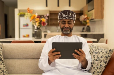 إنجاز مهام العمل عن بعد في المنزل, ايماءات الفرح والسعادة، استخدام الأجهزة التقنية والتكنولوجية الحديثة، التواصل والدردشة مع الأصدقاء والأقارب عبر الجوال، رجل كبير بالسن عربي خليجي عماني يرتدي الدشداشة والعمامة يمسك بيده التابليت المحمول يجلس في غرفة المعيشة إنجاز مهام العمل عن بعد في المنزل, ايماءات الفرح والسعادة، استخدام الأجهزة التقنية والتكنولوجية الحديثة، التواصل والدردشة مع الأصدقاء والأقارب عبر الجوال، رجل كبير بالسن عربي خليجي عماني يرتدي الدشداشة والعمامة يمسك بيده التابليت المحمول يجلس في غرفة المعيشة