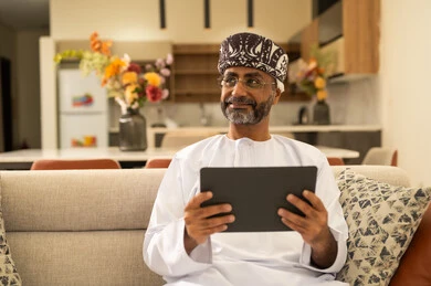 التواصل والدردشة مع الأصدقاء والأقارب عبر الجوال، إنجاز مهام العمل عن بعد في المنزل, ايماءات الفرح والسعادة، استخدام الأجهزة التقنية والتكنولوجية الحديثة، رجل كبير بالسن عربي خليجي عماني يرتدي الدشداشة والعمامة يمسك بيده التابليت المحمول يجلس في غرفة المعيشة التواصل والدردشة مع الأصدقاء والأقارب عبر الجوال، إنجاز مهام العمل عن بعد في المنزل, ايماءات الفرح والسعادة، استخدام الأجهزة التقنية والتكنولوجية الحديثة، رجل كبير بالسن عربي خليجي عماني يرتدي الدشداشة والعمامة يمسك بيده التابليت المحمول يجلس في غرفة المعيشة