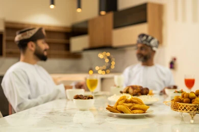 لمة الاصدقاء على سفرة رمضان, صديقان عربيان خليجيان عمانيان يرتديان الدشداشة والعمامة يقومان بتناول الطعام بايماءات السعادة و السرور بقدوم الشهر الفضيل, الاحتفال بالاعياد و المناسبات الاسلامية, اجتماع العائلة على المائدة