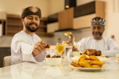 لمة الاصدقاء على سفرة رمضان, صديقان عربيان خليجيان عمانيان يرتديان الدشداشة والعمامة يقومان بتناول الطعام بايماءات السعادة و السرور بقدوم الشهر الفضيل, الاحتفال بالاعياد و المناسبات الاسلامية, اجتماع العائلة على المائدة