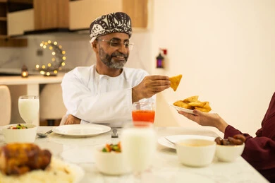 أجواء عائلية روحانية دينية إسلامية, فطور رمضاني عائلي، حسن الضيافة وإكرام الأخرين, موعد كسر الصيام عند أذان المغرب في رمضان المبارك، عائلة عربية خليجية عمانية تجلس بايماءات السرور, اجتماع الأسرة حول مائدة الإفطار المليئة بأصناف المأكولات والمقبلات الشهية