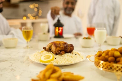 أجواء عائلية روحانية دينية إسلامية, فطور رمضاني عائلي، حسن الضيافة وإكرام الأخرين, موعد كسر الصيام عند أذان المغرب في رمضان المبارك، عائلة عربية خليجية عمانية تجلس بايماءات السرور, اجتماع الأسرة حول مائدة الإفطار المليئة بأصناف المأكولات والمقبلات الشهية