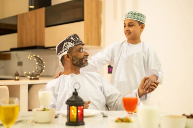 Hospitality and honoring others, the family gathering around the iftar table filled with various delicious dishes and appetizers, a family atmosphere that is spiritual and religiously Islamic, a family Ramadan breakfast, the time to break the fast at the call to prayer at sunset during the blessed month of Ramadan, an Arab Gulf Omani family sitting with gestures of joy.