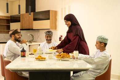 The time to break the fast is at the call to prayer for Maghrib during the blessed month of Ramadan. A family Ramadan iftar, an Arab Gulf Omani family sits with gestures of joy, hospitality, and honoring others. A spiritual and religious Islamic family atmosphere, the family gathers around the iftar table filled with a variety of delicious dishes and appetizers.