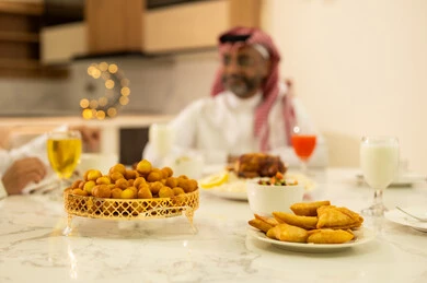 أصناف المأكولات والمقبلات الشهية، رجل يرتدي الثوب والشماغ التقليدي يجلس على مائدة الافطار مع عائلته , فطور رمضاني عائلي، موعد كسر الصيام عند أذان المغرب في رمضان المبارك، عائلة عربية خليجية سعودية تجلس بايماءات السرور