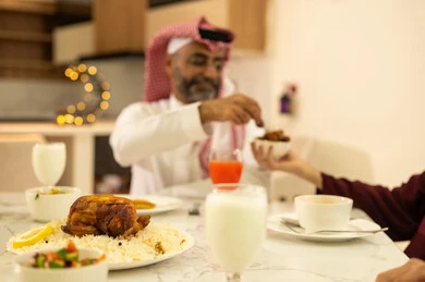 فطور رمضاني عائلي، أصناف المأكولات والمقبلات الشهية، رجل يرتدي الثوب والشماغ التقليدي يجلس على مائدة الافطار مع عائلته , موعد كسر الصيام عند أذان المغرب في رمضان المبارك، عائلة عربية خليجية سعودية تجلس بايماءات السرور