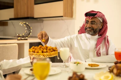 Expressions of joy and happiness, a family Ramadan breakfast, a variety of delicious dishes and appetizers, a man wearing the traditional thobe and shemagh sitting at the iftar table with his family, the time to break the fast at the call to prayer at sunset during the blessed month of Ramadan, a Saudi Gulf Arab family sitting with gestures of joy.