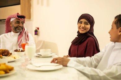 أجواء رمضانية سعيدة, بهجة الإفطار مع العائلة في شهر رمضان, عائلة عربية خليجية سعودية يرتدون الثوب التقليدي يجلسون على مائدة الطعام , تشكيلة متنوعة من الأطعمة الشهية، زينة واكسسوارات شهر رمضان المبارك