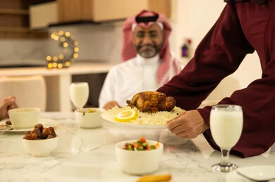 Happy Ramadan atmosphere, the joy of breaking the fast with family during the month of Ramadan, a Saudi Gulf Arab family wearing traditional attire sitting at the dining table, a variety of delicious foods, decorations, and accessories for the blessed month of Ramadan.