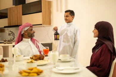 شهر الخير والبركة، المأكولات والمقبلات الرمضانيه المتنوعه والشهية، عائلة عربية خليجية سعودية على مائدة الافطار فى شهر رمضان الكريم في المنزل، ابن يرتدي الثوب السعودي التقليدي يحمل فانوس رمضان، اجواء وزينة واكسسوارات رمضانية، قضاء وقت ممتع مع الأسرة