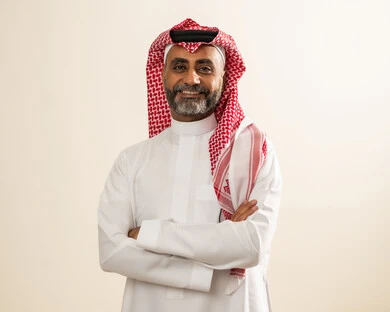 صورة شخصية للوثائق الرسمية، مفهوم الوسامة والاناقة، الاهتمام بالمظهر الخارجي ، بورتريه لرجل كبير بالسن عربي خليجي سعودي يرتدي الثوب والشماغ التقليدي يقف بأيدي متقاطعة وينظر إلى الكاميرا بإيماءات السعادة والسرور، خلفية بيضاء