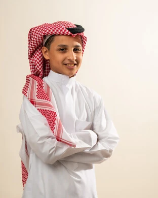 النظر إلى الكاميرا بإيماءات السعادة والسرور، صورة شخصية للوثائق الرسمية، مفهوم الوسامة والاناقة، الاهتمام بالمظهر الخارجي ، بورتريه لولد عربي خليجي سعودي يرتدي الثوب والشماغ التقليدي يقف بأيدي متقاطعة ، خلفية بيضاء