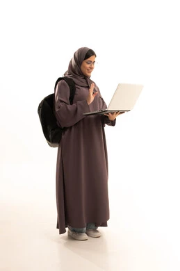 رفع كف اليد بتعابير القاء التحية ورد السلام, ، تبادل الأخبار مع الأهل والأصدقاء، بورترية لطالبة عربيه خليجيه سعودية ترتدي الحجاب و العباءة و حقيبة الظهر المدرسية تقوم بإجراء مكالمة فيديو باستخدام الحاسب المحمول، الجسم بالطول الكامل، خلفية بيضاء