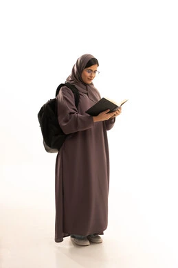 Spending free time learning and self-educating, gestures of attention and focus while reading, a portrait of a Gulf Arab Saudi student wearing a hijab and abaya with a school bag, reading attentively, exploring entertaining picture stories, developing reading skills, focusing on browsing useful books, full-body, white background.