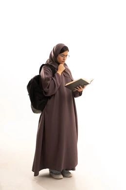 إيماءات الانتباه والتركيز بالمطالعة، تمضية أوقات الفراغ بالتعلم والتثقف الذاتي, بورتريه لطالبة عربية خليجية سعودية ترتدي الحجاب و العباءة و الحقيبة المدرسية تقوم بالقراءة بتمعن , مطالعة القصص التصويرية المسلية, تنمية مهارات القراءة , الاهتمام بتصفح الكتب المفيدة، الجسم بالطول الكامل، خلفية بيضاء