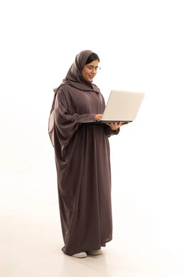 Browsing the internet and using modern technology devices, a portrait of a young Arab Saudi Gulf woman wearing a hijab and abaya using a laptop to accomplish tasks, managing and organizing business affairs, full-body shot, white background.