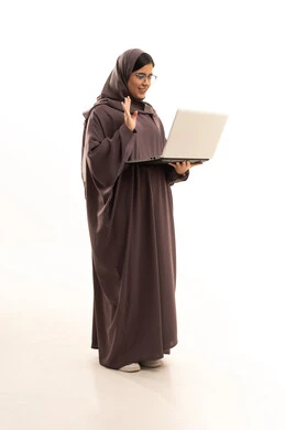 Greeting through video calls, a portrait of a young Saudi Arabian Gulf woman wearing a hijab and abaya using a laptop to complete tasks, managing and organizing business affairs, browsing the internet and using modern technological devices, full-body shot, white background.