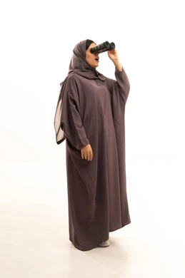 التخطيط المستقبلي للأهداف و الطموحات، حب الاستكشاف والمغامرة، بوتريه امرأة عربية سعودية خليجية محجبة تمسك بيدها منظار ثنائي العينين ( التلسكوب ), الرؤية بالعدسة المكبرة , ايماءات وجه تدل على الذهول والدهشة , الجسم بالطول الكامل، خلفية بيضاء