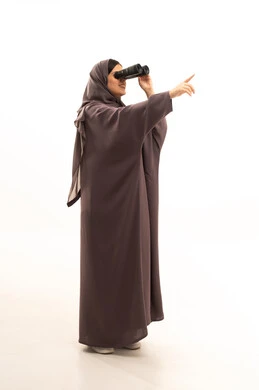 إيماءات وتعابير وجه تدل على الاستمتاع, التخطيط المستقبلي للأهداف و الطموحات، حب الاستكشاف والمغامرة، بورتريه لإمرأة عربية خليجية سعودية تنظر من خلال منظار الرؤية وتشير بيدها الى شيء ما, رؤية الاشياء البعيدة عبر المنظار، الجسم بالطول الكامل، خلفية بيضاء